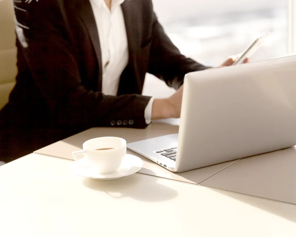 Restaurant manager working on laptop with coffee, reviewing restaurant marketing strategy and customer engagement in a modern hospitality setting.