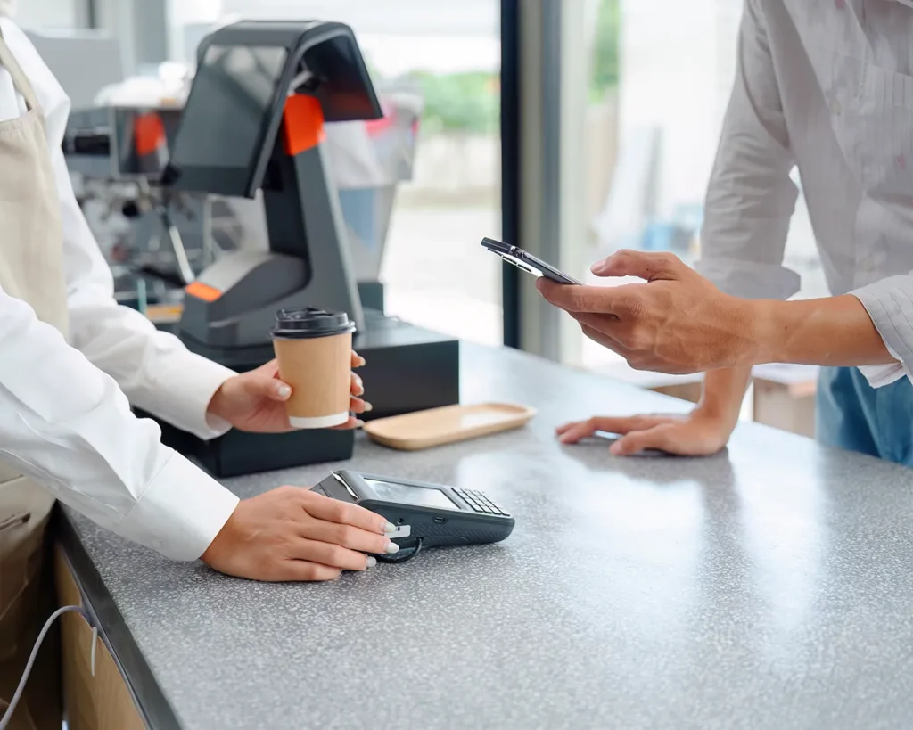 Customer paying with smartphone at a café counter, showcasing web-based restaurant loyalty program, digital rewards, and contactless payment.