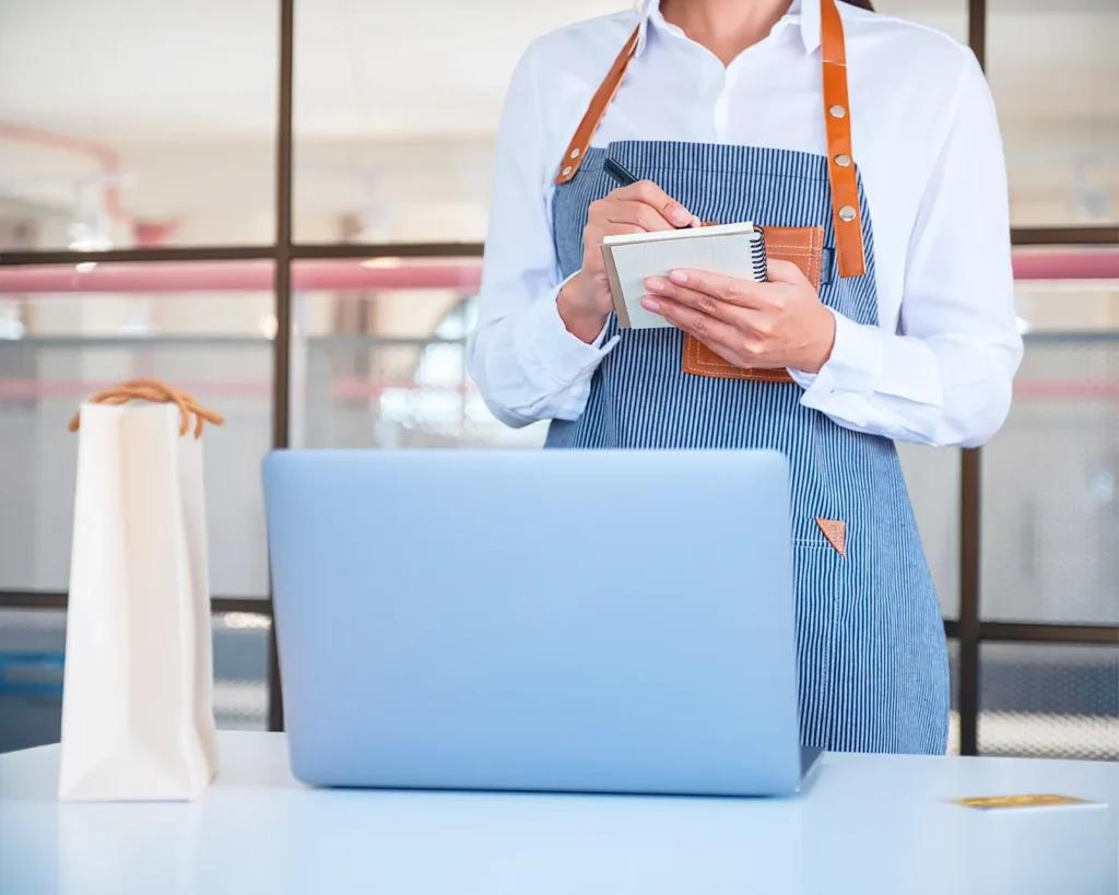 Restaurant manager taking notes on customer insights and loyalty program strategy beside laptop