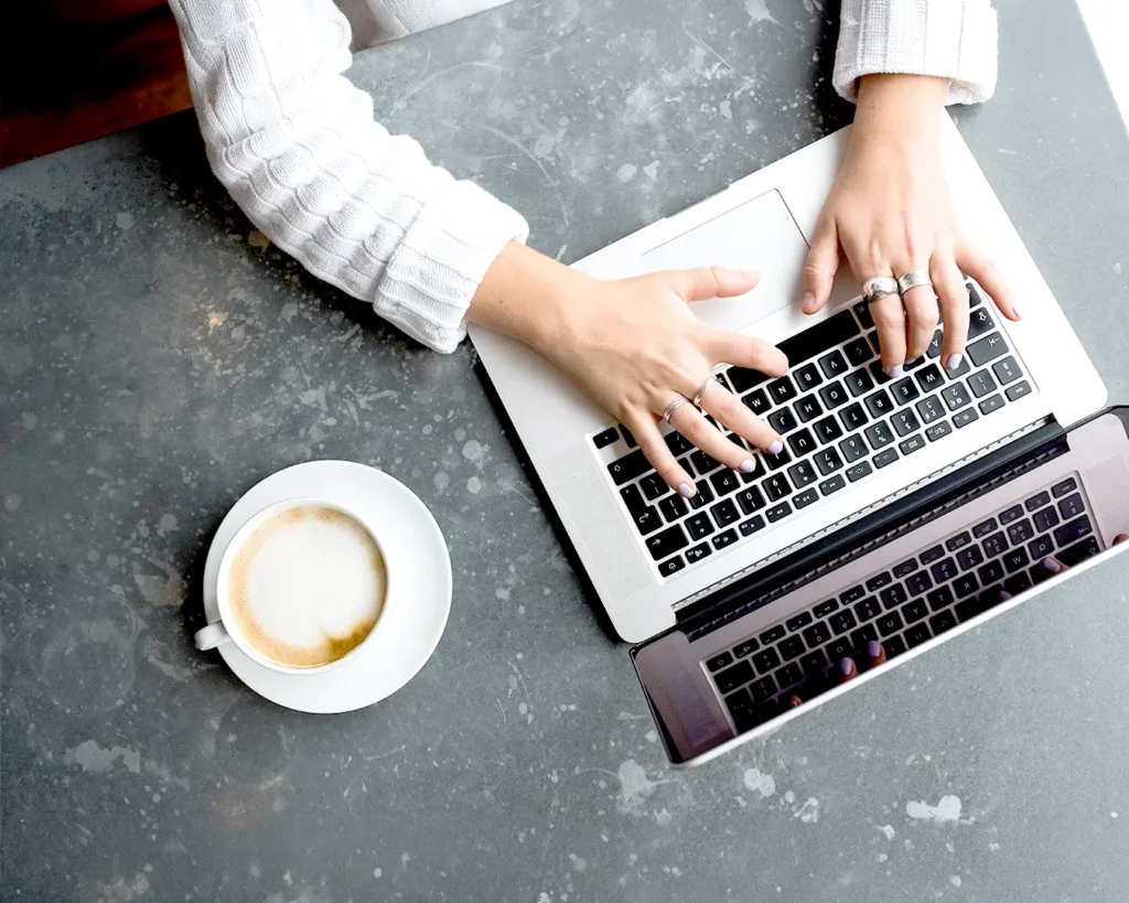 Restaurant owner typing on laptop beside coffee, managing automated restaurant promotions, email marketing, and customer database.
