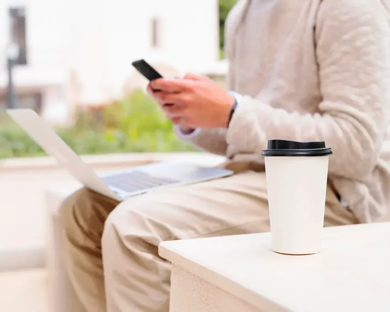 Mobile ordering customer using smartphone and laptop in modern café setting for restaurant app and web ordering comparison