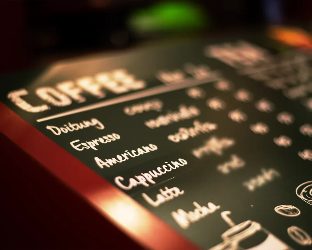Close-up of a restaurant menu featuring coffee drinks including espresso, americano, and cappuccino