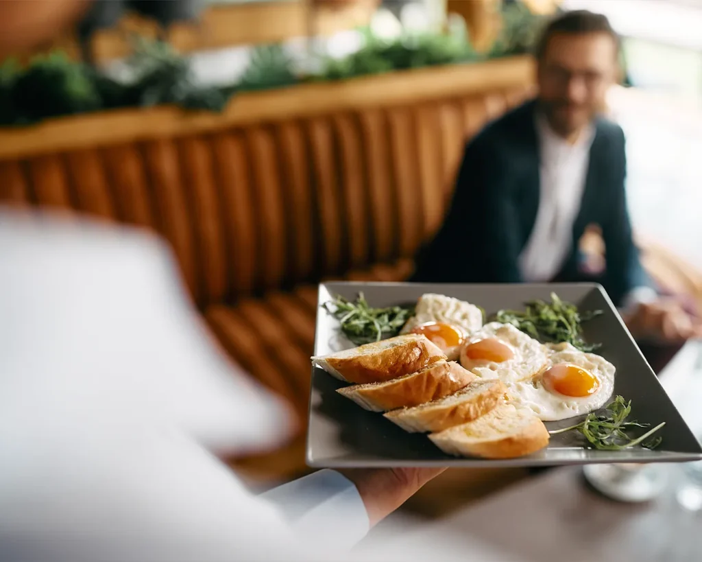 Server presenting a plated breakfast dish to restaurant guest