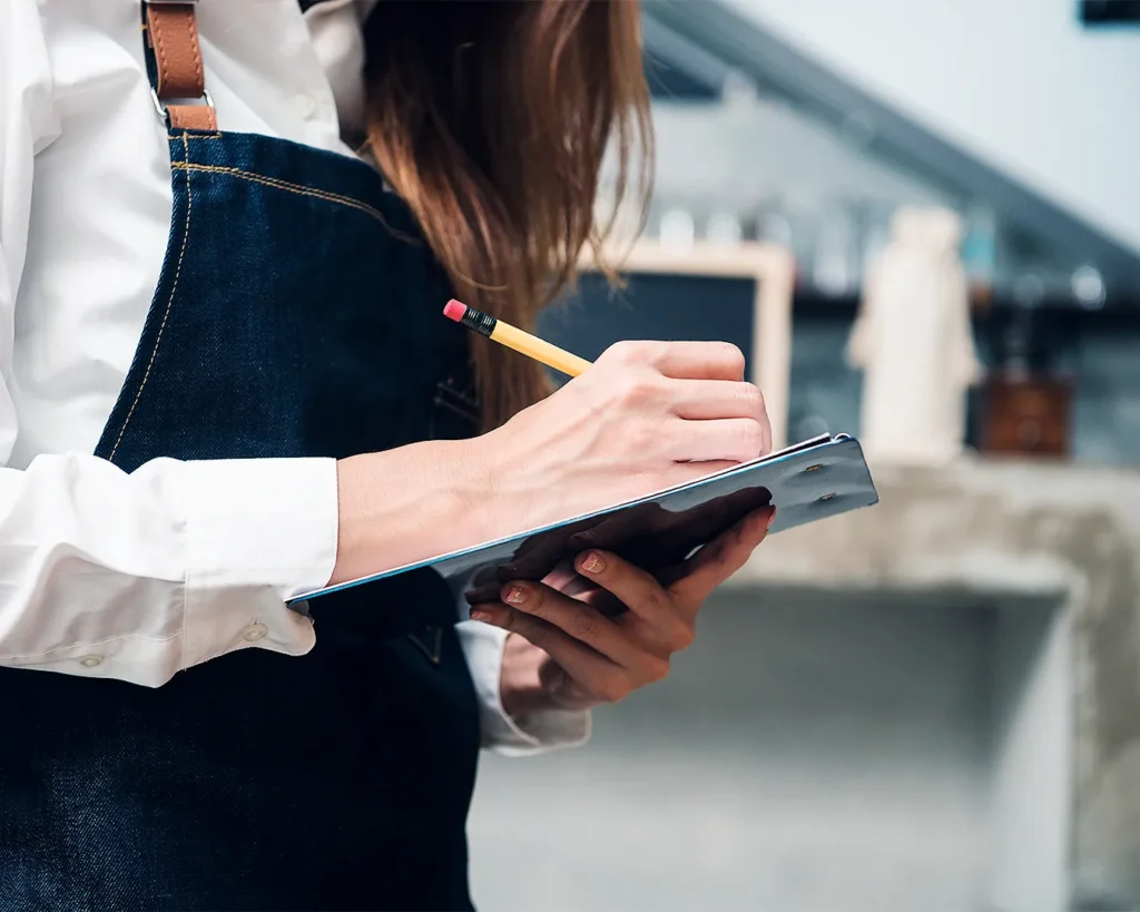 Restaurant server taking customer feedback and dining notes on clipboard during service