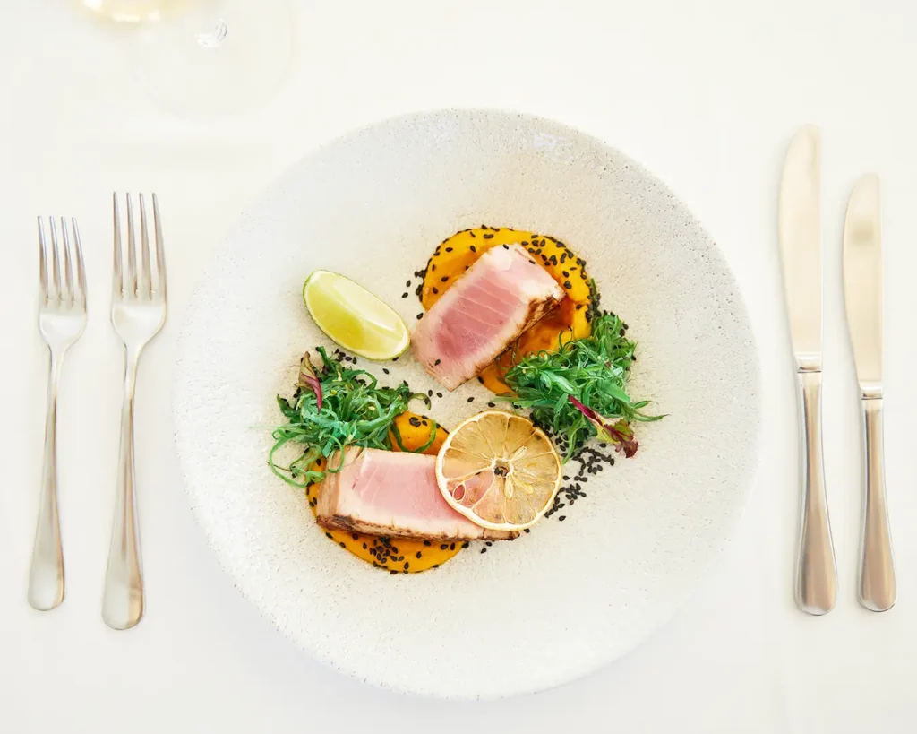 Gourmet tuna dish with roasted vegetables, sesame seeds, herbs, and citrus garnish