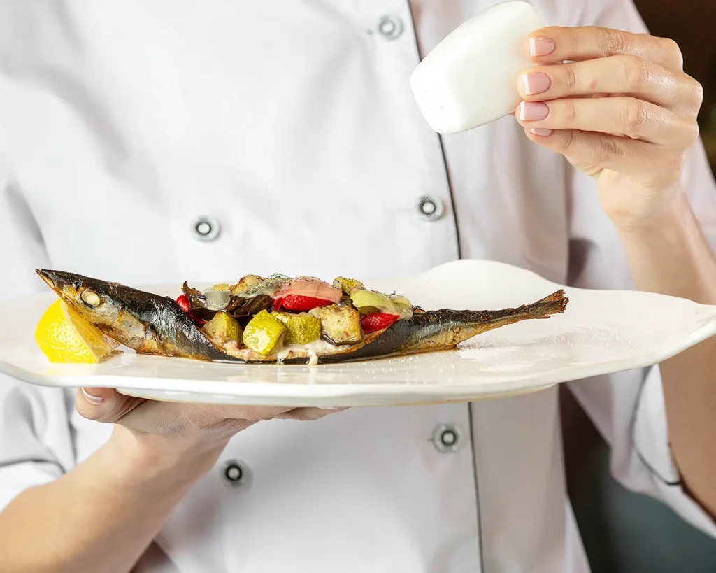 Chef presenting a seasonal fish dish with fresh vegetables and lemon garnish
